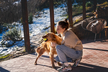Young adult happy woman playing with her retriever dog on the terrace of a country house in early spring - 751562339