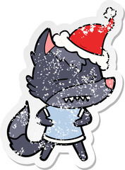 distressed sticker cartoon of a wolf showing teeth wearing santa hat