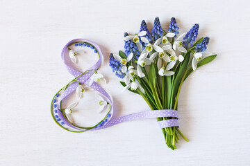 Wooden white background with a bouquet of spring flowers snowdrops and muscari, ribbon in the shape of the number eight. Postcard for Women's Day March 8th. - 751567728
