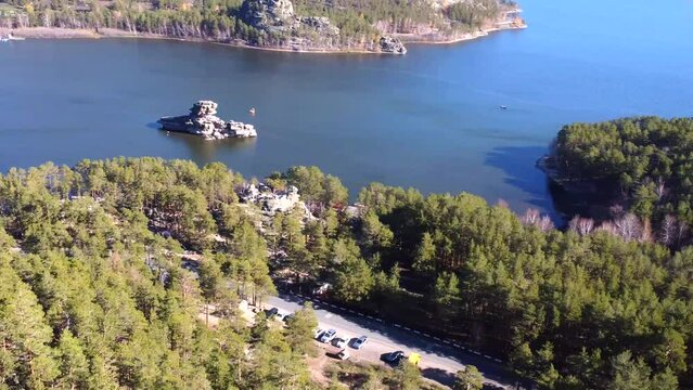 An aerial view of the amazing nature of Kazakhstan, behind a huge rock there is a view of the turquoise Lake Burabay with the Zhumbaktas rock surrounded by coniferous trees. Atmospheric journey.