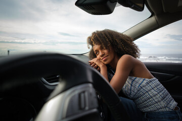 Woman relaxing inside a car looking through the window towards the sea.