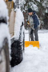A man is shoveling snow off the ground. He is wearing a black hat and a blue jacket