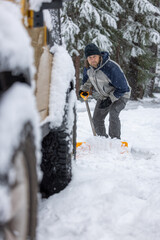 A man is shoveling snow off the road. The snow is piled up on the ground and the man is using a shovel to clear it