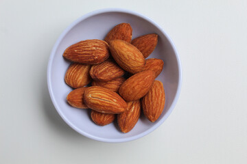 Roasted almond in small white bowl, isolated on white background, top view or flat lay