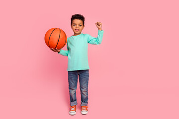 Naklejka premium Full size photo of charming small boy hold basketball ball raise fist wear trendy aquamarine outfit isolated on pink color background