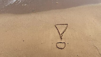 Exclamation mark writing on beach sand on blue water waves background. Top view.