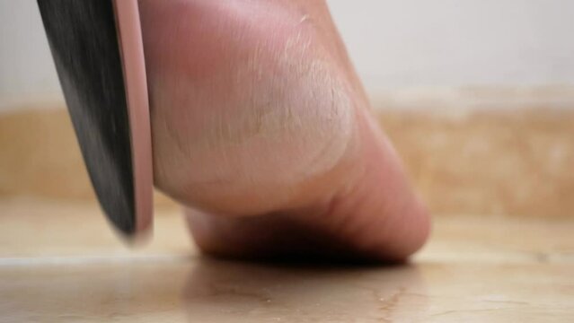Woman using foot file for removing dead skin from feet at home, woman scrubbing foot process by pumice