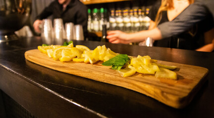 Sliced fresh lemons artistically presented on a wooden board in a bar setting, with bartenders in...