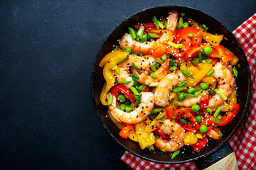 Hot stir fry shrimps with colorful paprika, green peas, chives and sesame seeds with ginger, garlic and soy sauce.   Black kitchen table background, top view