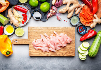 Food and cooking background. Wooden cutting board with chopped chicken slices. Paprika, zucchini,...