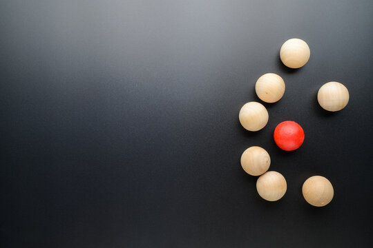Small red ball is under seige of many wooden balls on black background, small business in competition, and enciclement, or niche, and different concept