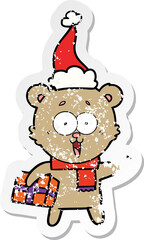 Fototapeta premium laughing teddy bear with christmas present wearing santa hat