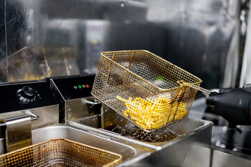 person in black gloves lifts a basket of freshly fried food from a commercial deep fryer. Droplets...