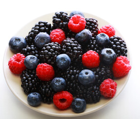 Various fresh berries on plate isolated on white background. Raspberry, Blueberry, Blackberry.
