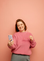 Portrait of surprised woman talking by mobile phone over pink background