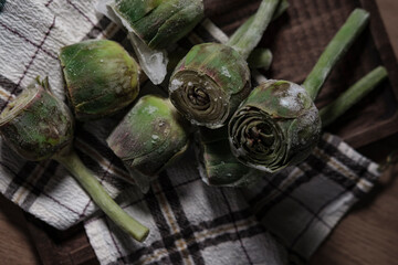 fresh frozen baby artichoke buds raw on kitchen cloth textle, wooden board, dark rustic colors,...