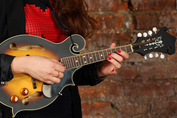 Female hands hold and play mini guitar in studio with red brick wall