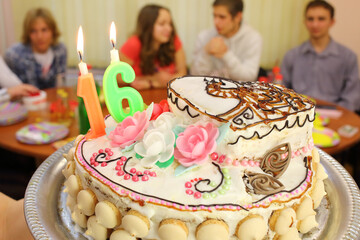 Beautiful festive birthday cake with candles sixteen on a tray against four teenagers in the classroom