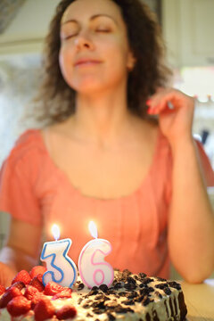 Woman makes a wish before blowing candle in shape of number thirty six on cake, focus on candles