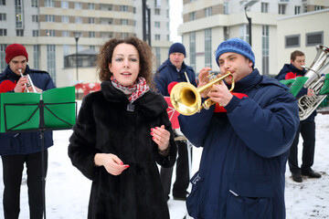 Brass band of four musicians play and woman sings outdoor at winter day