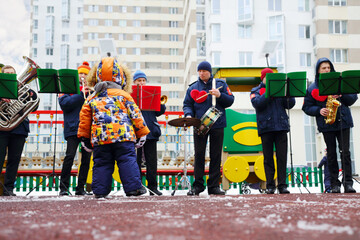 Brass band of six musicians play outdoor at winter day and kid listens their on playground