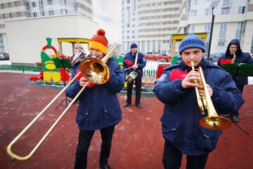 Brass band of five musicians play near building on playground at winter day