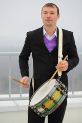 Man in black suit plays drum on roof of tall building at winter day