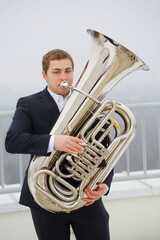 Man in black suit plays tuba on roof of tall building at winter day