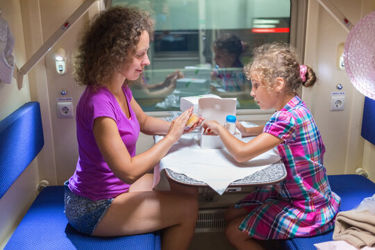 Mother and daughter eat, sitting in bench at table near window of moving speed train