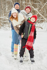 Smiling family of four stands on skates on ice pathway in winter park
