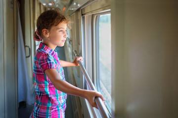 Young girl standing inside train and pensively looking out window