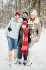 Happy family of four stands embracing on skates on ice pathway in winter park