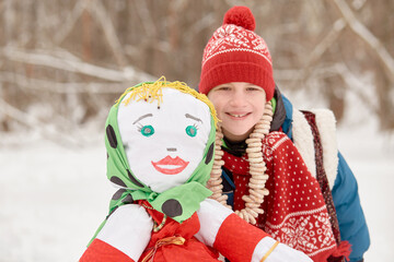 Smiling boy stands near stuffed dummy Maslenitsa in winter park