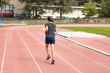Obraz premium Back view of a young woman running on a stadium track; back view of a young woman jogging on a running track.