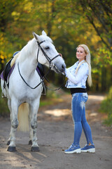 Woman with white hair stands near white horse in sunny autumn park