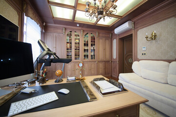 Interior of the modern cabinet in the English style with desktop, wooden bookcase and white sofa