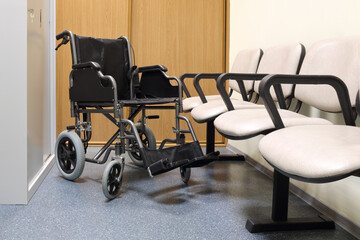 Black wheel chair stands in lobby of hospital ready to transport patient