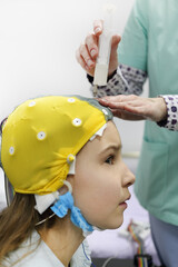Nurse using syringe introduces special gel for electrodes located in cap of electroencephalogram, girl looking to side, focus on syringe - obrazy, fototapety, plakaty