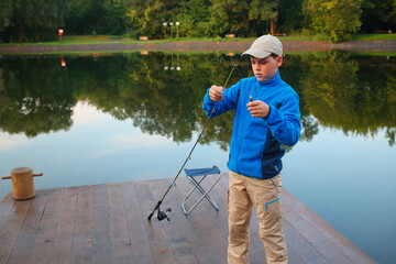 Young boy adjusts float rods on dock at river early morning