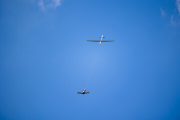 White glider plane being pulled by other small airplane towards the blue sky. Glider pulling on a sunny day.