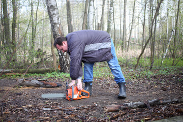 A man with glasses starts a chainsaw in the forest