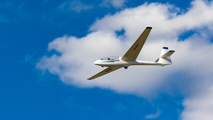 White glider plane against the blue sky. A shot of a glider airplane in flight on a sunny day.