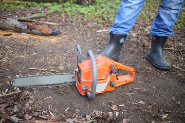 Chainsaw lying on the ground at the feet of men in rubber boots