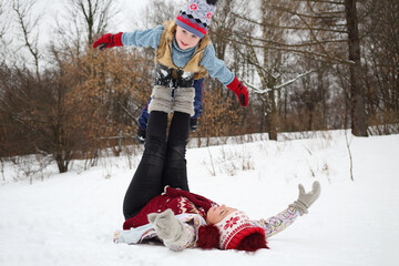 Woman lies on her back and holds little cute boy on feet in snow