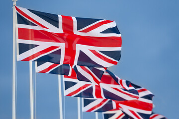 Row of Union Jack British Flags on Flagpoles Flying in a Blue Sky - 751624585