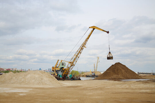 Cranes work at dock on River and huge piles of sand at spring day