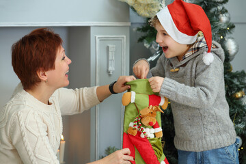 Happy boy takes out sock gift and mothre looks at he near christmas tree, focus on woman