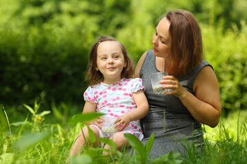 Little girl smiles and her mother with milk looks at she in sunny park