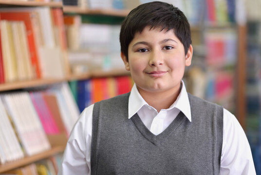 Pupil in grey jacket on background of shelves with books, smile and look at camera