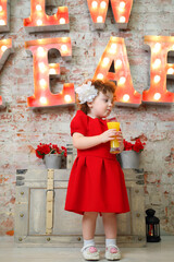 Little girl drinks juice near illuminated letters (New Year)